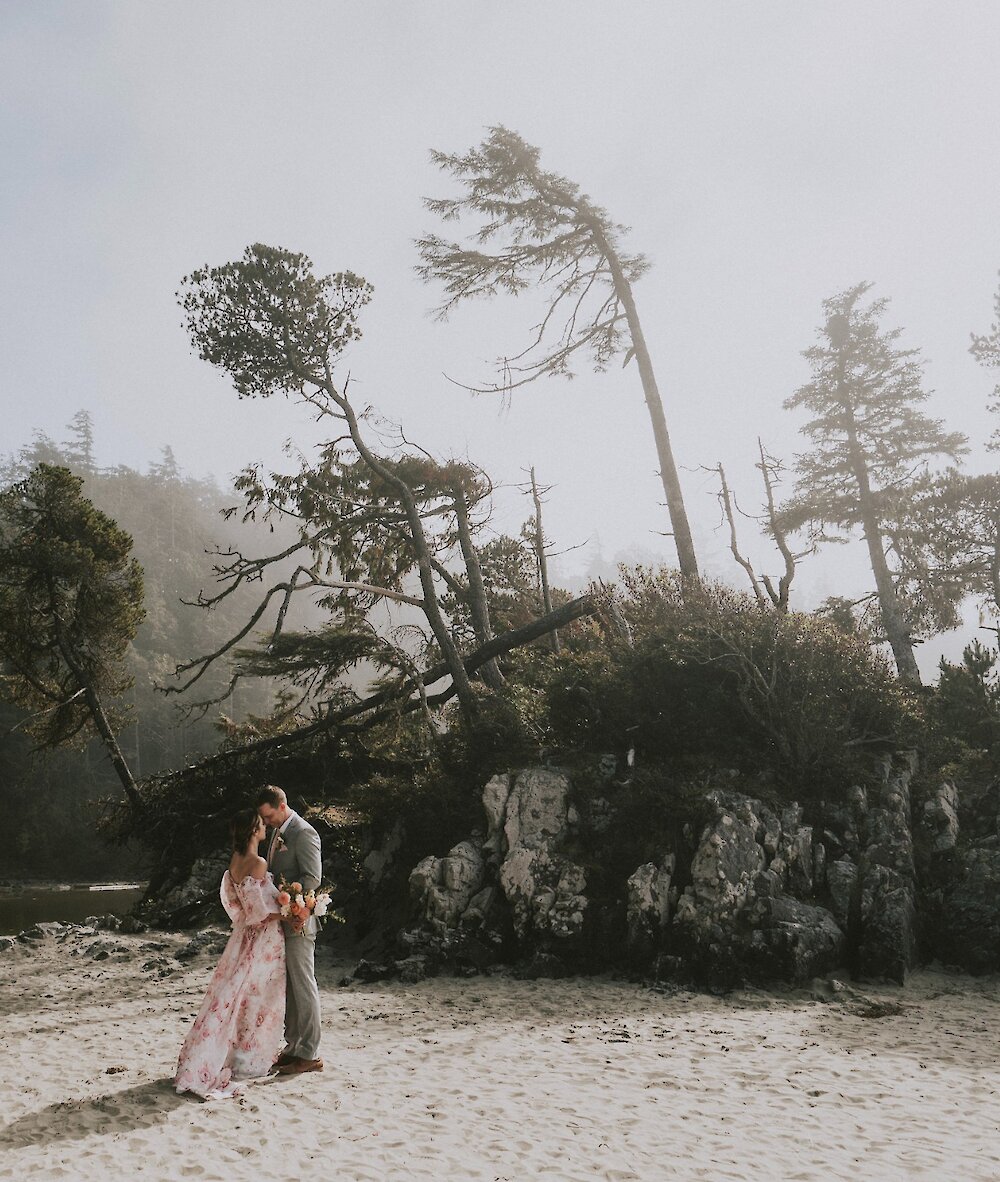 Two people standing near a small island on a misty Tonquin Beach.