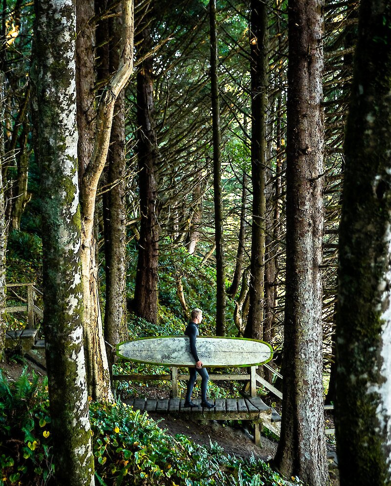Person walking down stairs in the forest to the beach with a surfboard