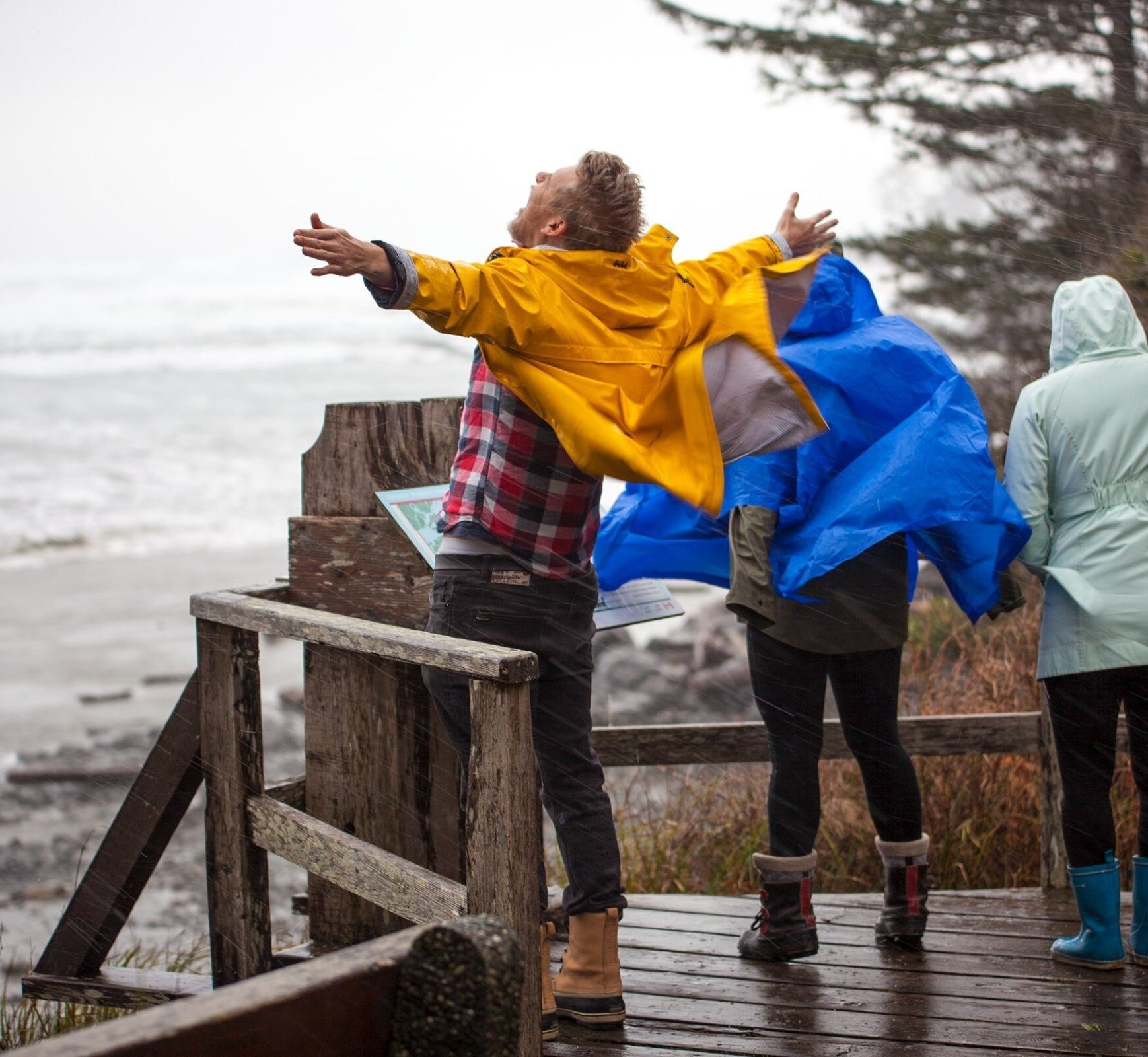 Person standing in the wind on a deck by the sea with arms outstretched