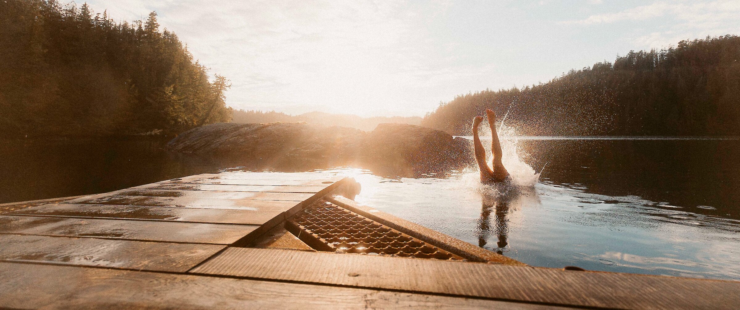 Person diving off a dock into the ocean in sunlight